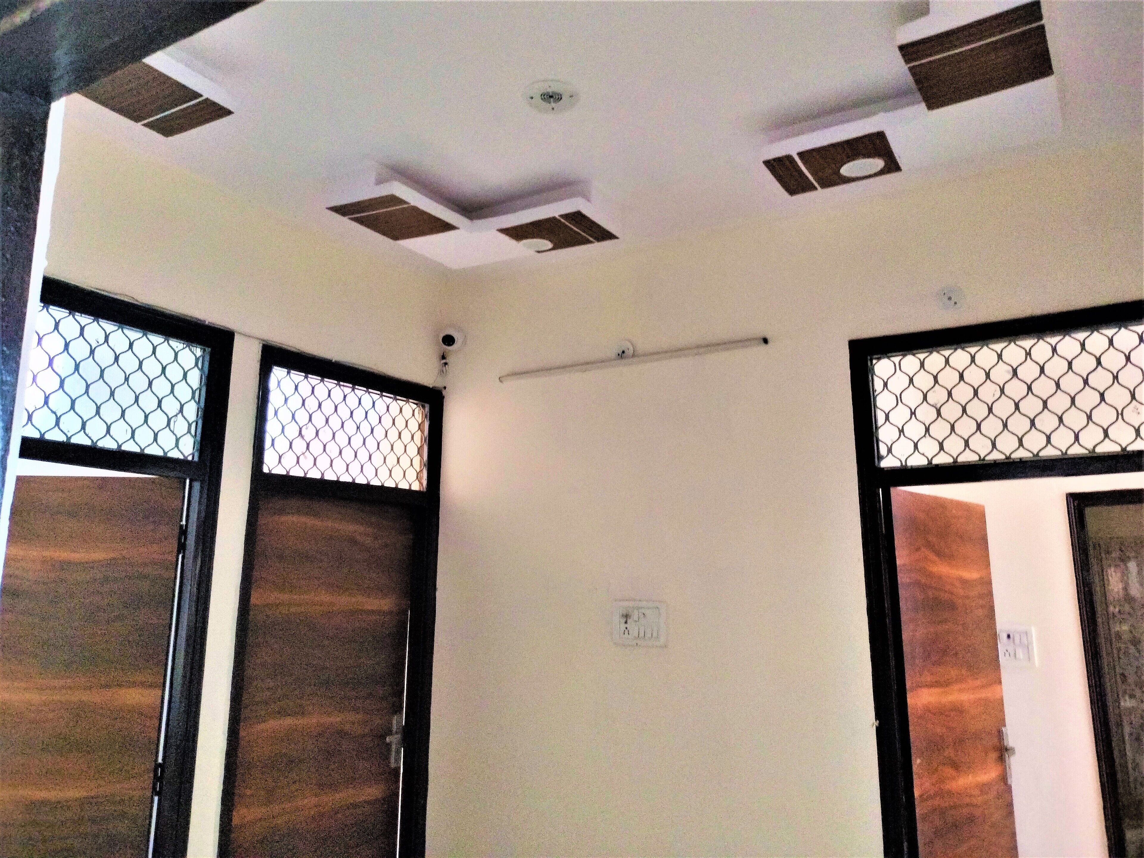 Une pièce dont le plafond est doté d’un éclairage encastré et d’un luminaire central. On y trouve deux portes avec des fenêtres à treillis métallique et une porte en bois à la finition marron.
