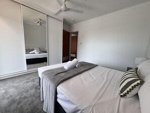 Habitación de hotel con una cama, un espejo, un ventilador de techo y una puerta que da a otra habitación.