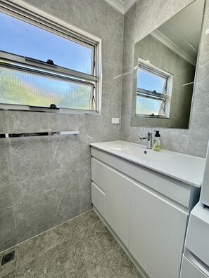 Un baño con un ventanal grande, un lavabo, un espejo y piso de baldosas.