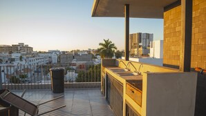 A rooftop terrace with a view of the city, a sink, a trash can, and a chair.