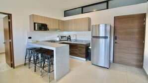 A modern kitchen with a central island, bar stools, a stainless steel refrigerator, and wooden cabinetry.
