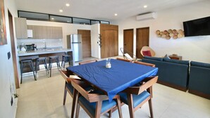 A modern kitchen with a dining area, a sofa, and a TV mounted on the wall.