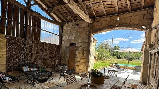 A rustic outdoor dining area with a stone wall, wooden furniture, and a view of the garden. - Charming country house with pool (Saint-Seurin-sur-l'Isle)