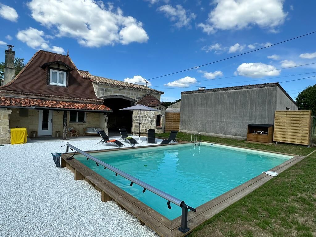 A swimming pool with a wooden deck, lounge chairs, and a stone building in the background.