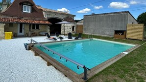A swimming pool with a wooden deck, lounge chairs, and a stone building in the background. - Charming country house with pool (Saint-Seurin-sur-l'Isle)