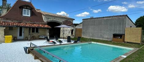 A swimming pool with a wooden deck, lounge chairs, and a stone building in the background.