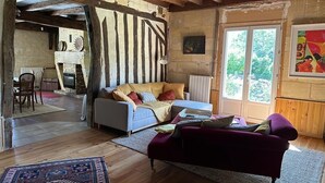 A rustic living room with exposed wooden beams, a fireplace, and a large window with a view of greenery. - Charming country house with pool (Saint-Seurin-sur-l'Isle)