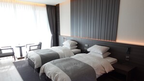 A modern hotel room with two beds, a small table, and a chair. - Pine Beach Golf Hotel (Haenam)