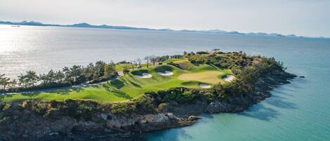Vista aérea de un campo de golf con búnkeres y una masa de agua.