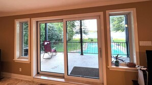 A room with large sliding glass doors leading to an outdoor patio with a pool and chairs. - Villa Delrose Waterfront (Montréal)