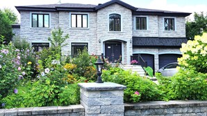 A two-story stone house with a black front door, multiple windows, and a car parked in the driveway. - Villa Delrose Waterfront (Montréal)