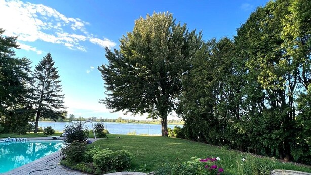 A paved walkway leading to a swimming pool, surrounded by lush greenery and trees. - Villa Delrose Waterfront (Montréal)
