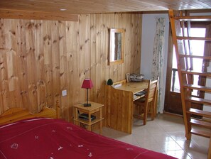 A wooden-paneled room with a bed, desk, chair, and a ladder.
