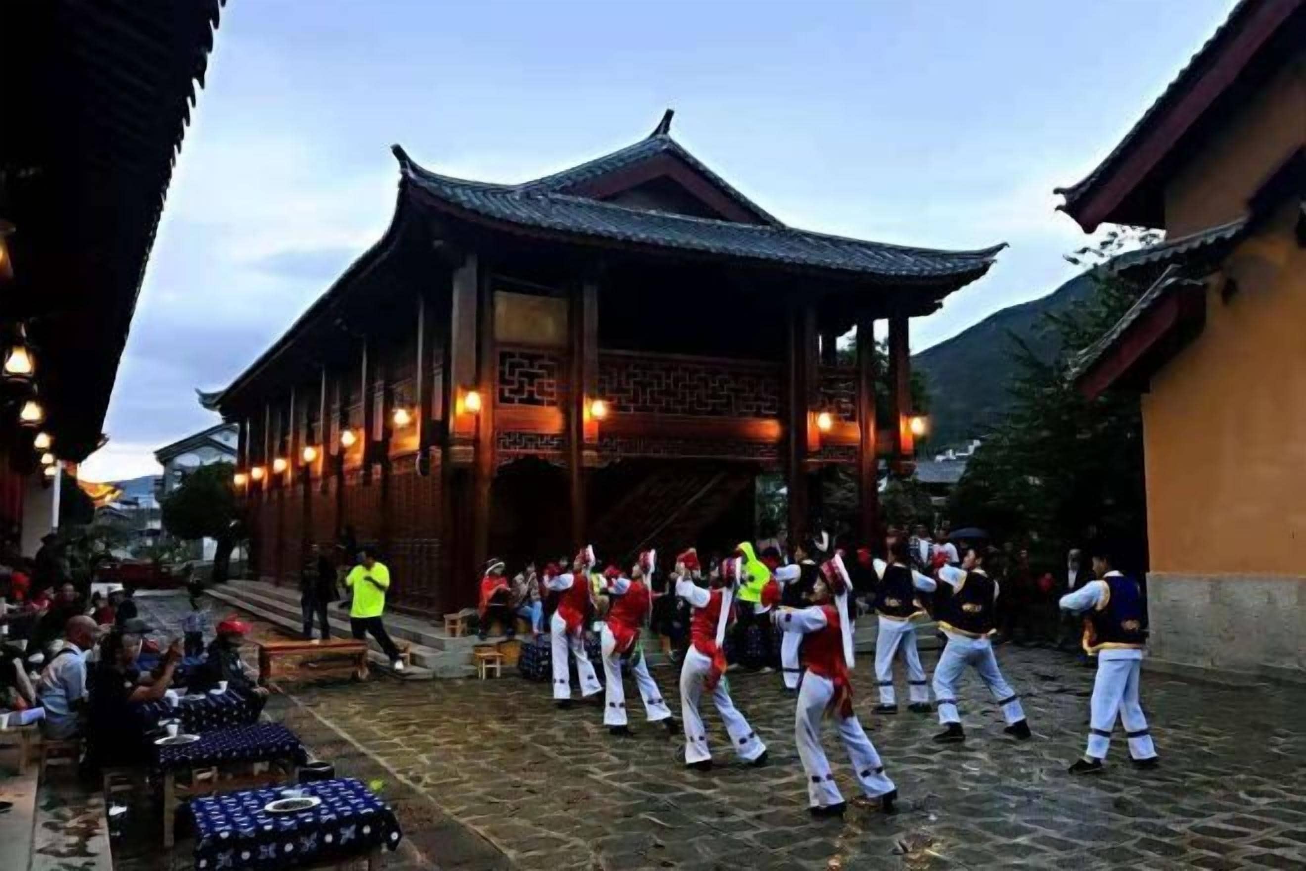 A traditional building with a tiled courtyard, a group of people performing a dance, and a person in a yellow vest.