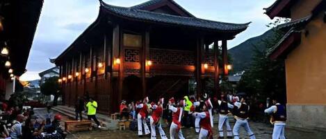 A traditional building with a tiled courtyard, a group of people performing a dance, and a person in a yellow vest.
