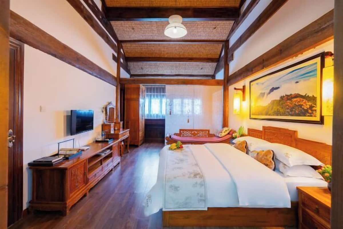 A bedroom with a bed, wooden furniture, a TV, and a painting.