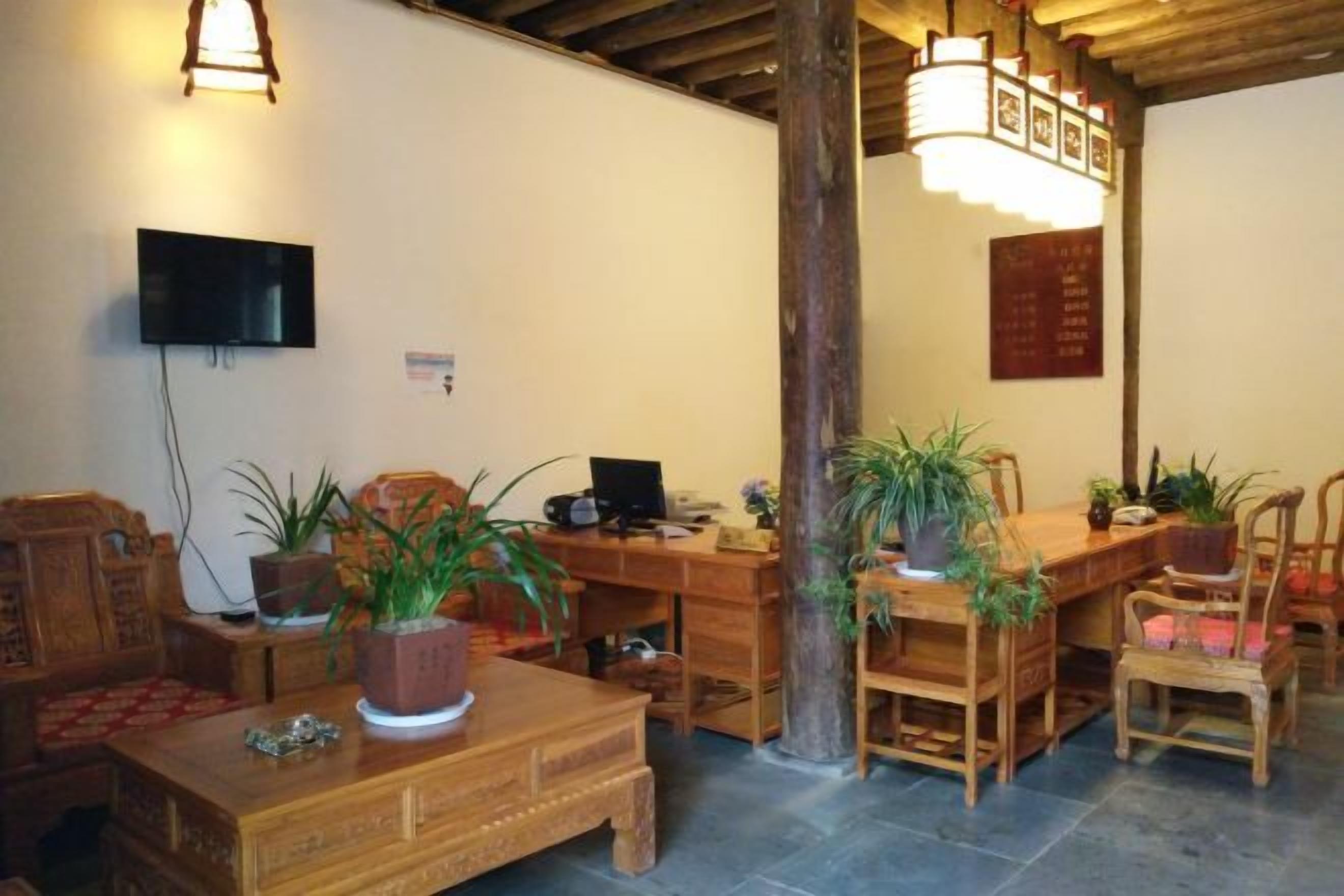 A room with a wooden coffee table, chairs, a desk, and a television mounted on the wall.