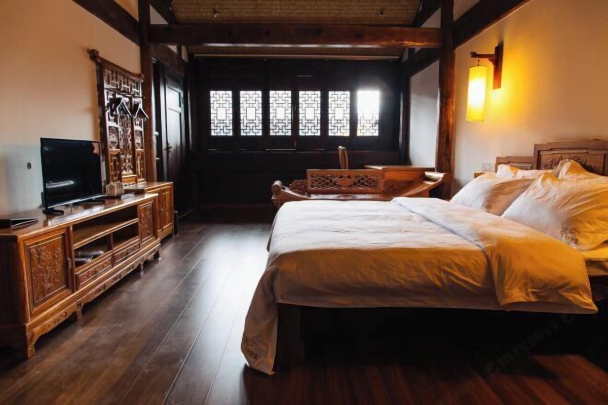 Ein traditionell eingerichtetes Zimmer mit einem großen Bett, Holzmöbeln und einem Fernseher.