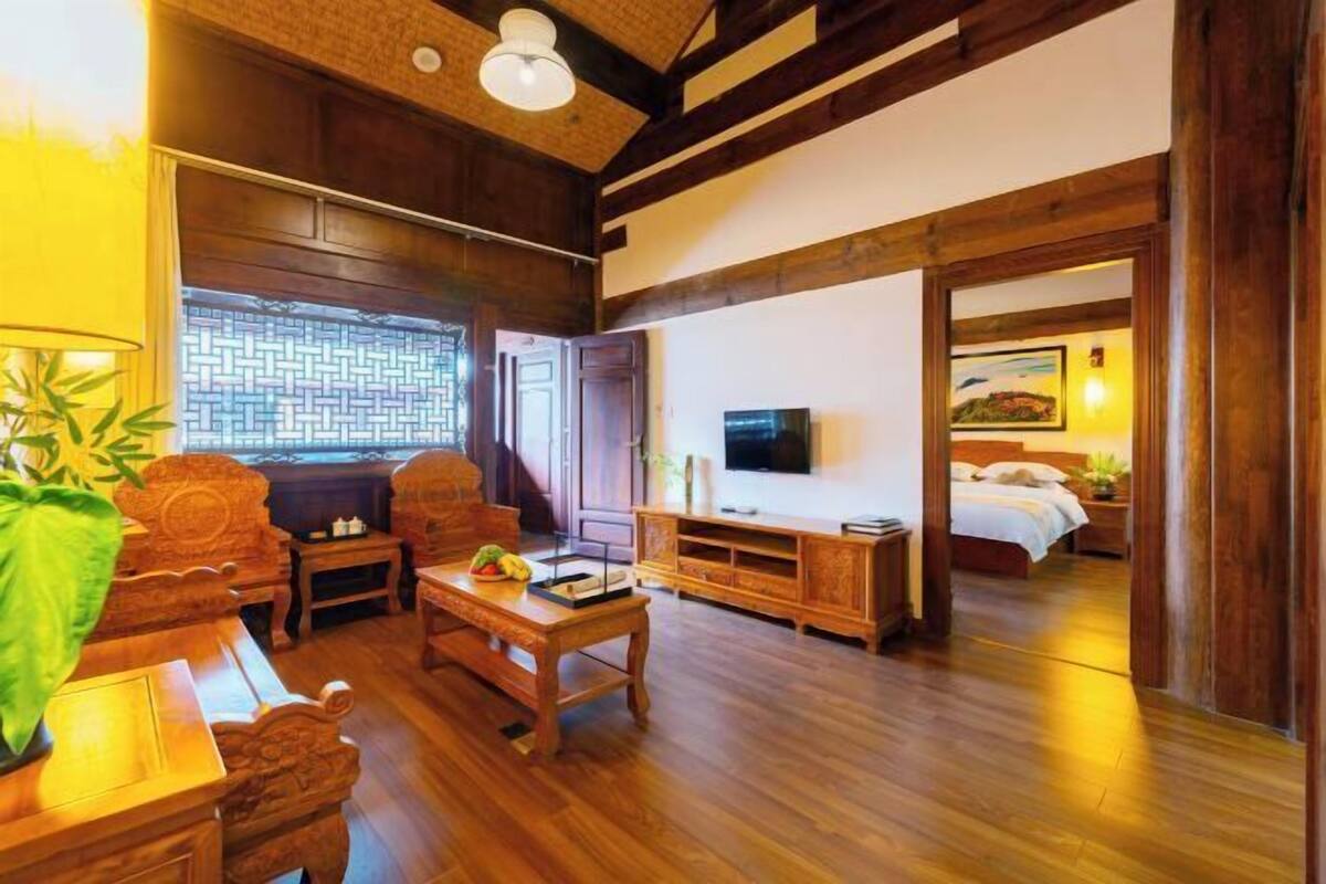 A room with a wooden floor, a sofa, a coffee table, a TV, and a bed.