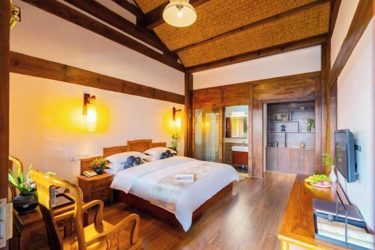 A bedroom with a wooden bed, bedside tables, a desk with a chair, and a television.