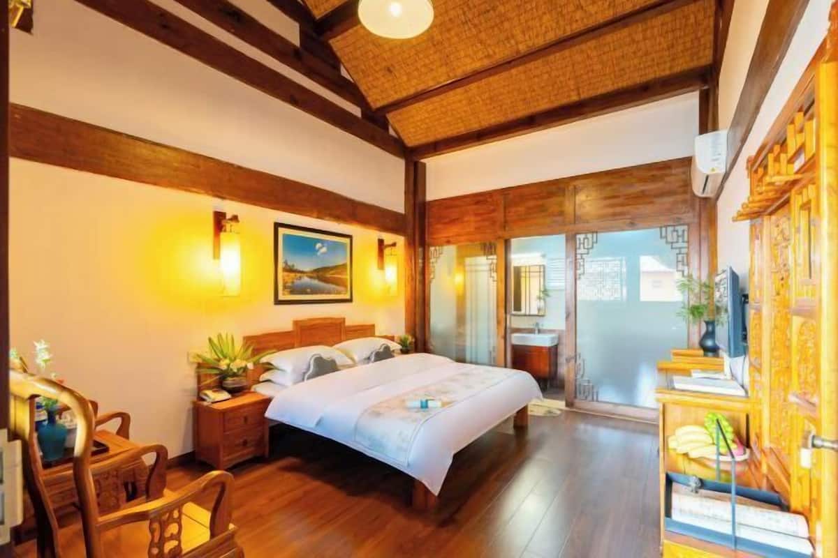 A bedroom with a wooden bed, bedside tables, a desk, and a chair. There is a window with a view of the outside.