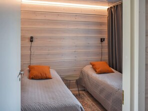 Une petite pièce compacte avec deux lits simples, chacun agrémenté d’un oreiller orange. Les murs sont en bois et une prise de courant est fixée au mur.
