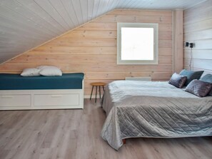 Un dormitorio con techo inclinado, una cama con cubrecama acolchado, un banco con cojines y un taburete pequeño.