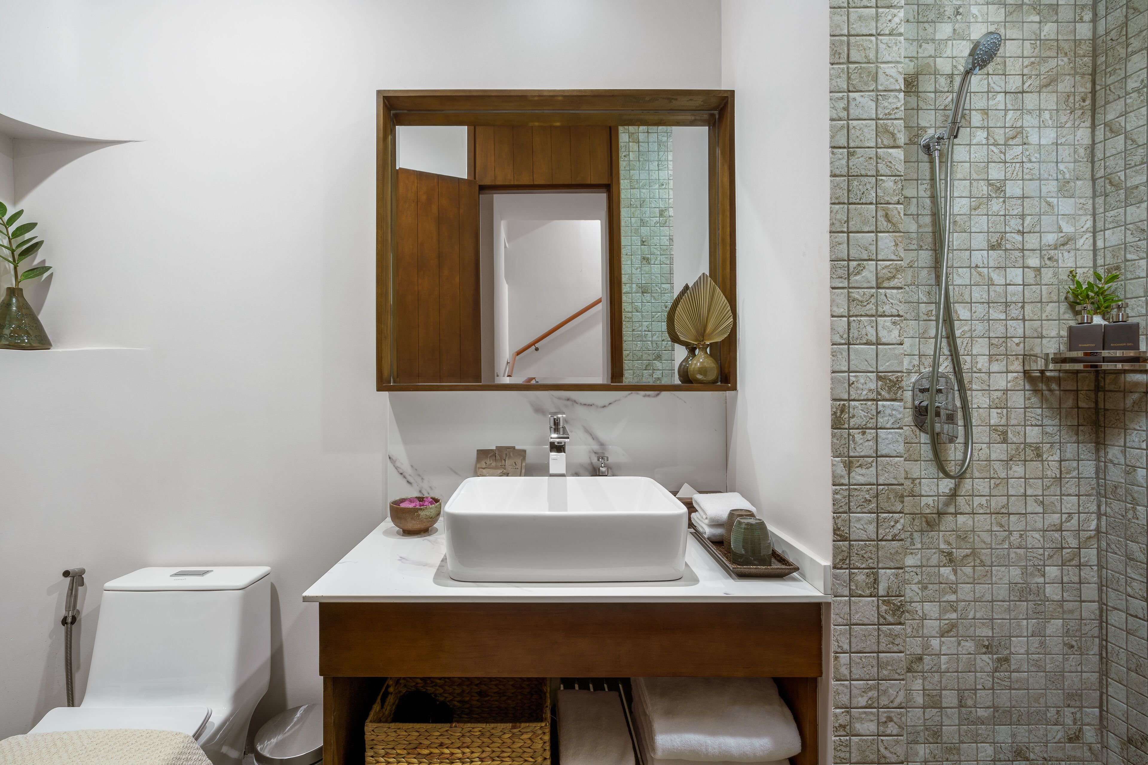 Une salle de bain moderne avec un lavabo blanc, un meuble-lavabo en bois, un miroir, une douche avec une porte en verre et un mur carrelé.