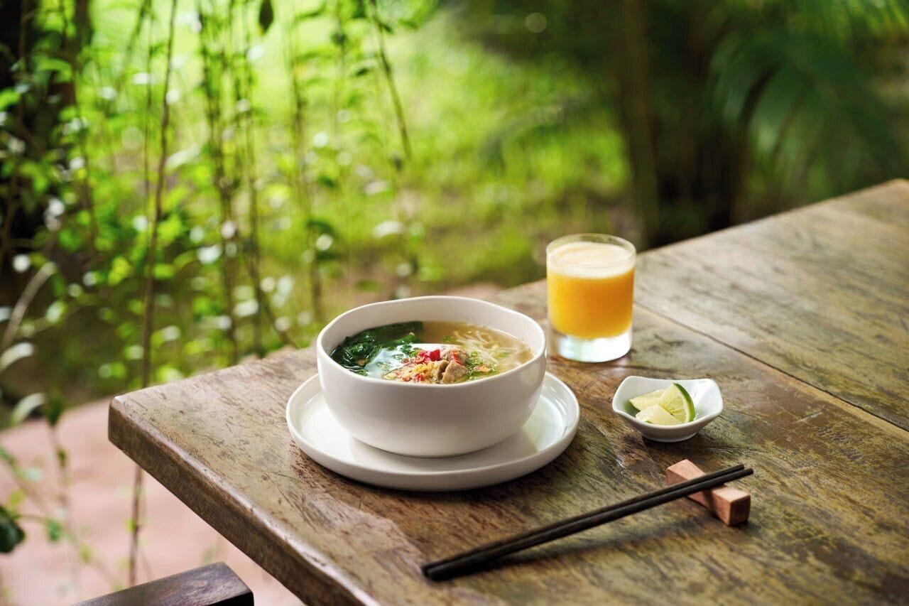 A bowl of soup on a wooden table with chopsticks and a glass of orange juice.