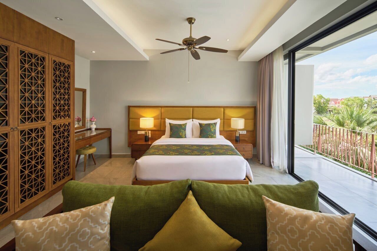 Habitación de hotel con una cama grande, dos lámparas de noche, un ventilador de techo y vistas al exterior.