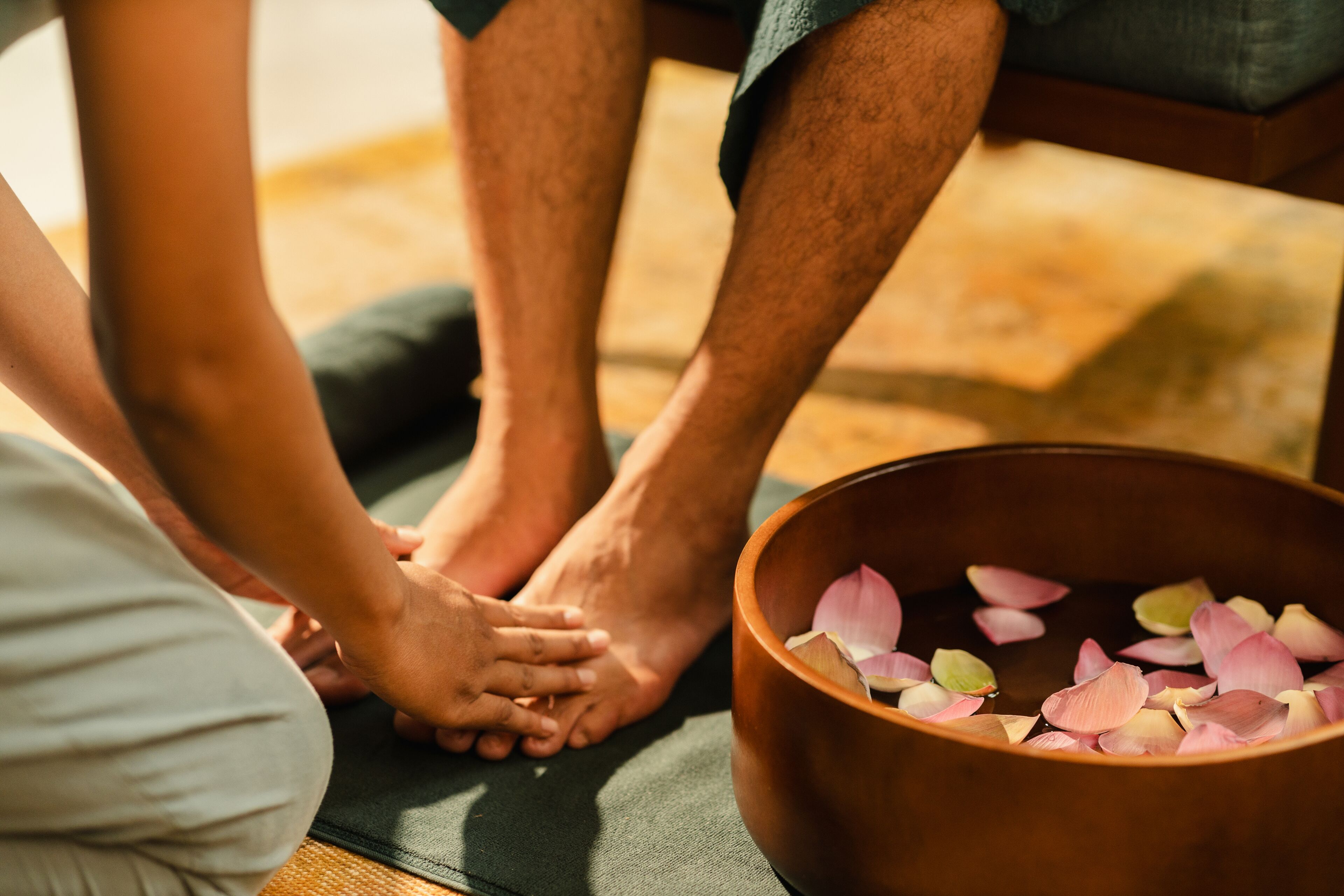A person receiving a foot massage with a bowl of rose petals nearby.