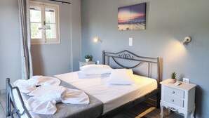 Ein ordentlich bezogenes Bett mit weißen Leinen und Kissen, ein Nachttisch mit Pflanze, ein Wandbild und ein Fenster mit Vorhängen.