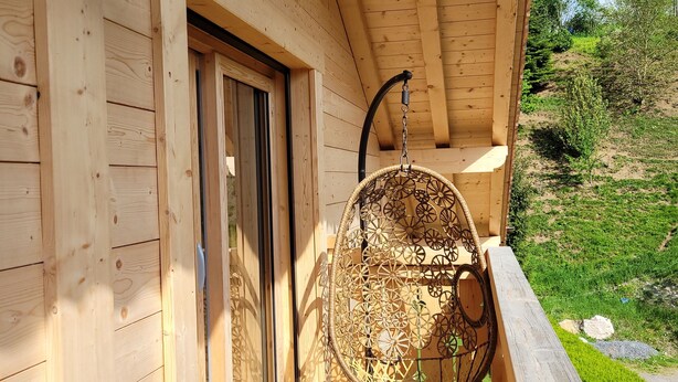 Une cabane en bois avec une véranda, un fauteuil suspendu et un luminaire fixé au mur.