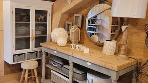 Une pièce mansardée chaleureuse avec des poutres apparentes, une armoire blanche aux portes vitrées, une table en bois agrémentée d’objets décoratifs et un miroir avec un cadre en bois.