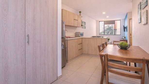 A modern kitchen with wooden cabinets, a dining table with chairs, and a window providing natural light.