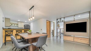 A modern kitchen with a dining area, a TV, and a built-in shelf unit.