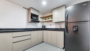 A kitchen with beige cabinets, a black countertop, a stainless steel refrigerator, and a microwave above the stove.