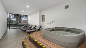 A modern indoor pool area with a hot tub, lounge chairs, and a glass door leading to an outdoor space. - Olive 404 · Penthouse 2 hab Dúplex-Jacuzzi privado en terraza (Alto Palmas)