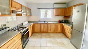 A kitchen with wooden cabinets, a gas stove, a refrigerator, and a window providing natural light. - Seaside House-Flic en Flac (Flic en Flac)