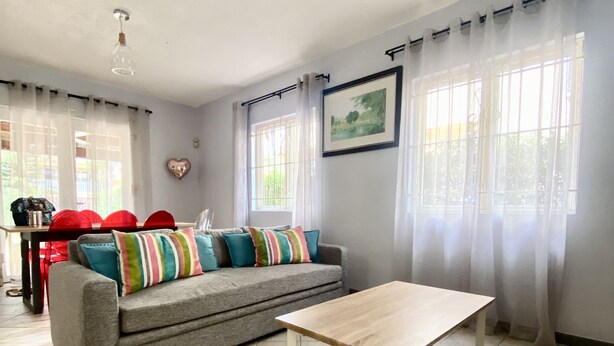 A living room with a grey sofa, a wooden coffee table, and a rug. There are two windows with curtains, a picture on the wall, and a ceiling light. - Seaside House-Flic en Flac (Flic en Flac)