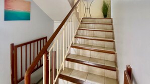 A staircase with wooden handrails and beige steps, leading to a landing with a window and a plant. - Seaside House-Flic en Flac (Flic en Flac)