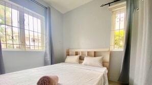 A neatly made bed with a rolled towel, a headboard, and a window with curtains. - Seaside House-Flic en Flac (Flic en Flac)
