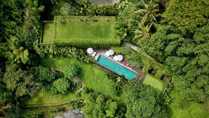 An aerial view of a lush, green landscape with a swimming pool surrounded by neatly trimmed hedges and palm trees. - Peaceful river and jungle views, 6 bedrooms, close to beaches. (Tabanan)