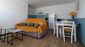 Un espace de vie compact comprenant un canapé, une petite table, un coin repas avec des chaises, un réfrigérateur, un four à micro-ondes et une lampe.