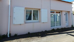 Un bâtiment doté de deux fenêtres, dont l’une est munie d’un rideau et l’autre d’un volet, et dont on peut voir la porte.