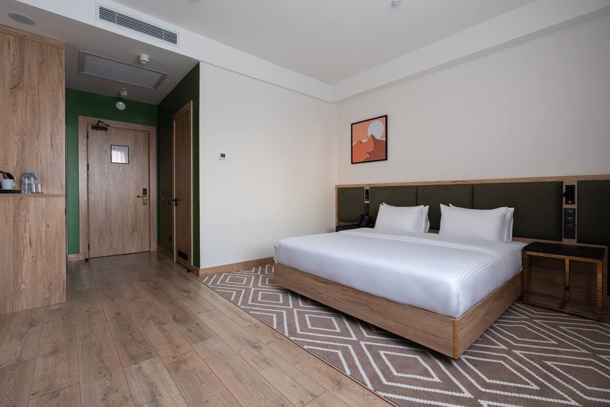 A hotel room with a wooden bed, a green wall, a painting, and a patterned rug.