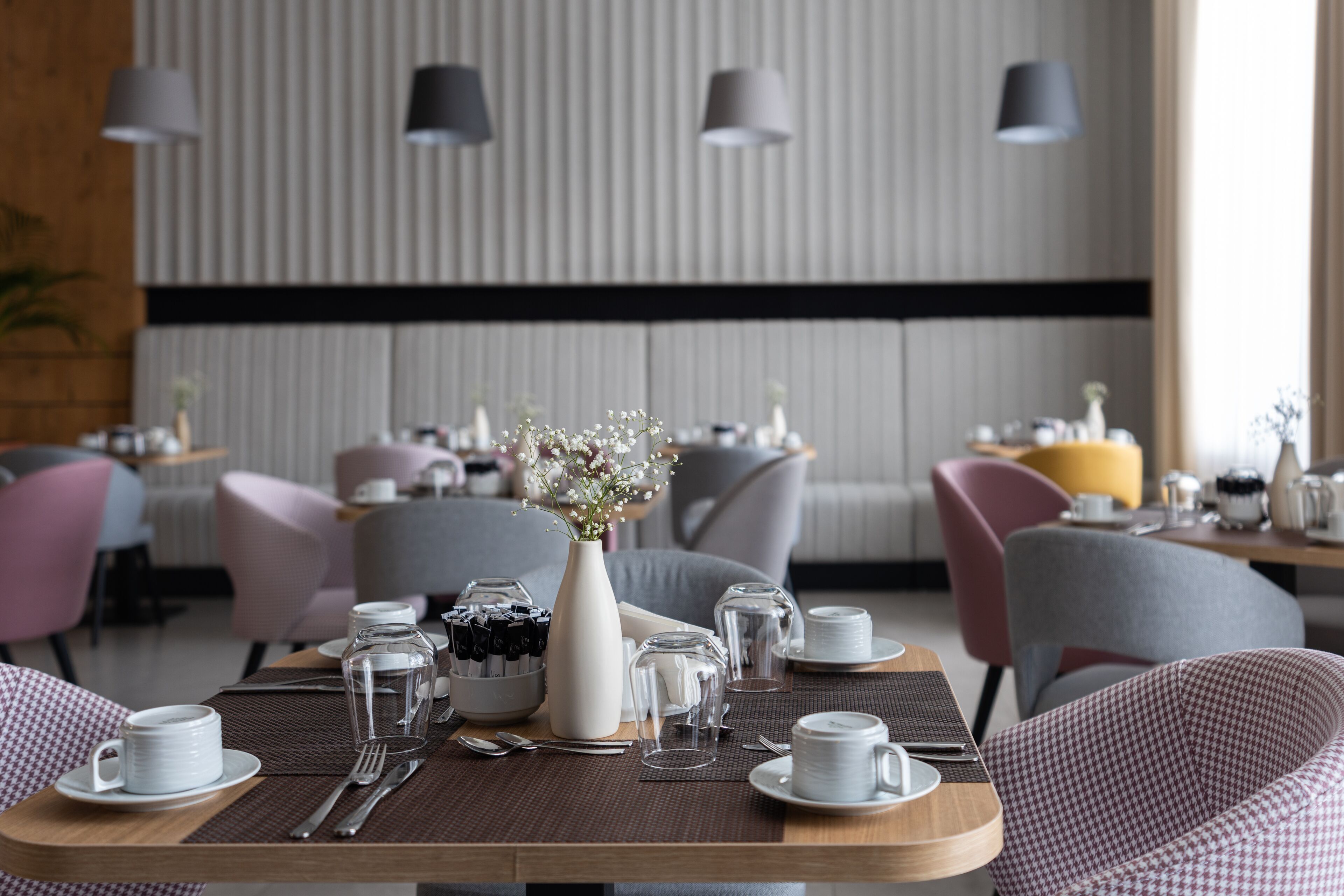 Un coin repas avec une table dressée pour deux personnes, agrémenté d’un vase de fleurs, de verres transparents et d’assiettes.
