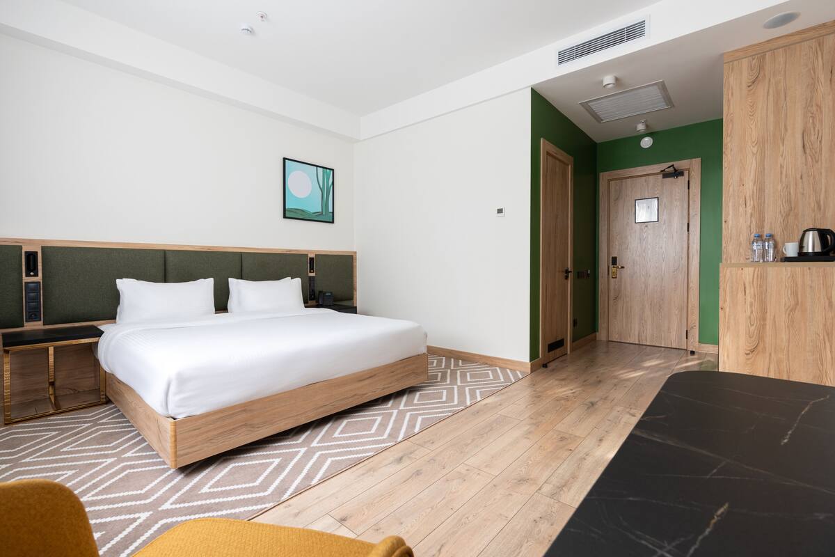 A modern hotel room with a wooden bed, a desk, and a wardrobe.