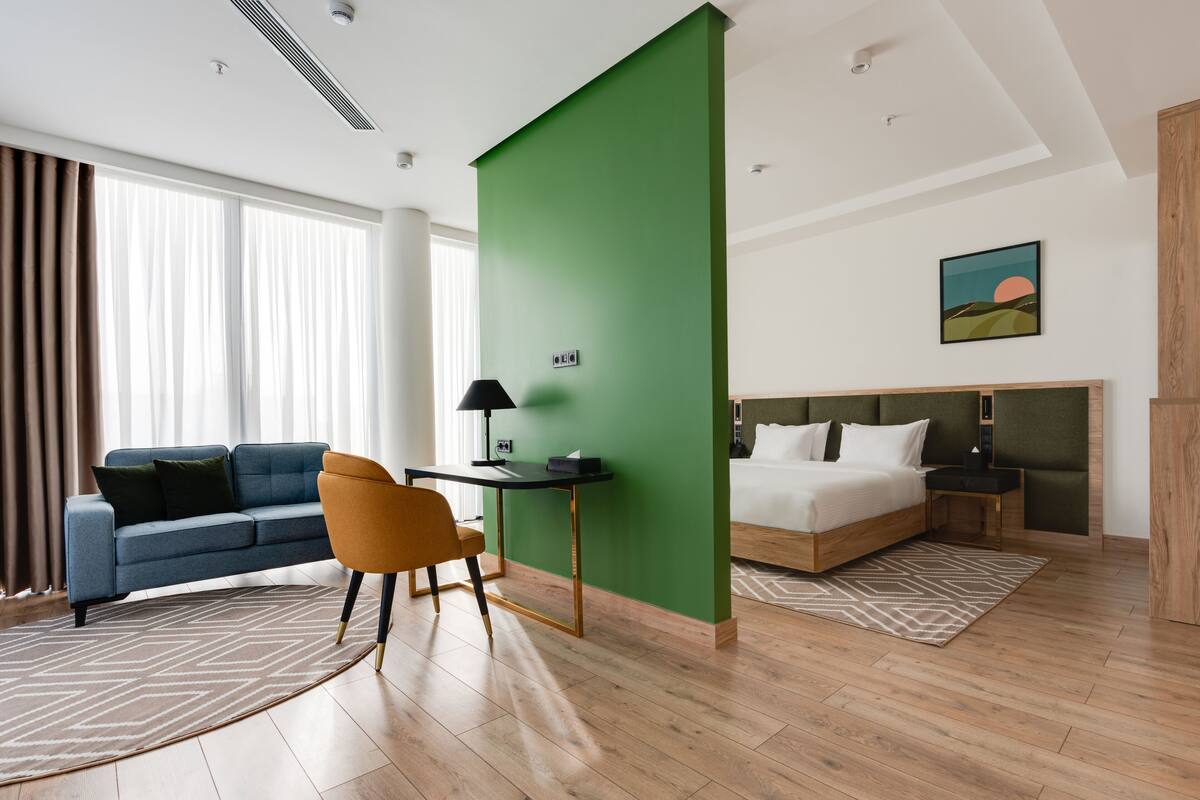 A modern hotel room with a bed, a desk, a chair, and a large window with curtains.