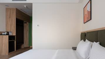 A modern hotel room with a large bed, a wooden wardrobe, a green accent wall, and a framed artwork above the bed.